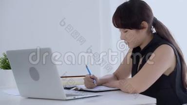 有笔记本电脑的女商人用计算器计算开支，并用计算器写笔记簿以节省开支